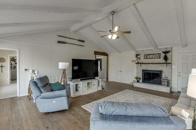 living room with ceiling fan, a large fireplace, hardwood / wood-style floors, and vaulted ceiling with beams