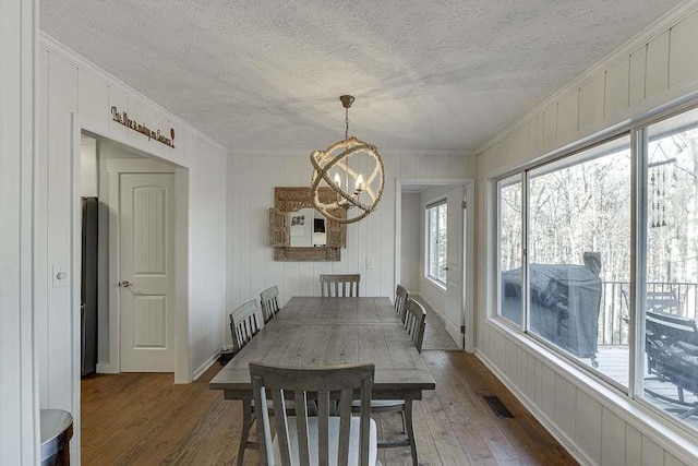 dining space with dark hardwood / wood-style flooring, a notable chandelier, ornamental molding, and a textured ceiling