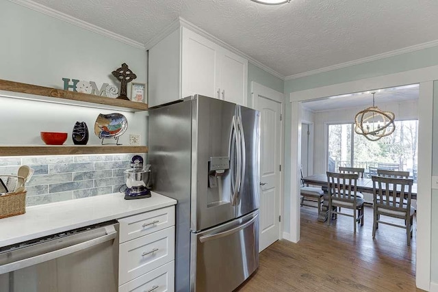 kitchen with pendant lighting, stainless steel appliances, ornamental molding, light hardwood / wood-style floors, and white cabinets