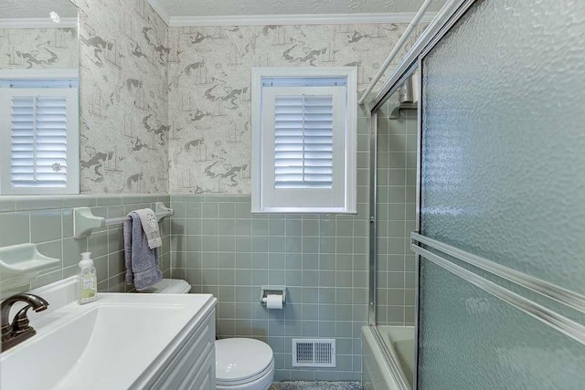 full bathroom featuring toilet, bath / shower combo with glass door, tile walls, ornamental molding, and vanity