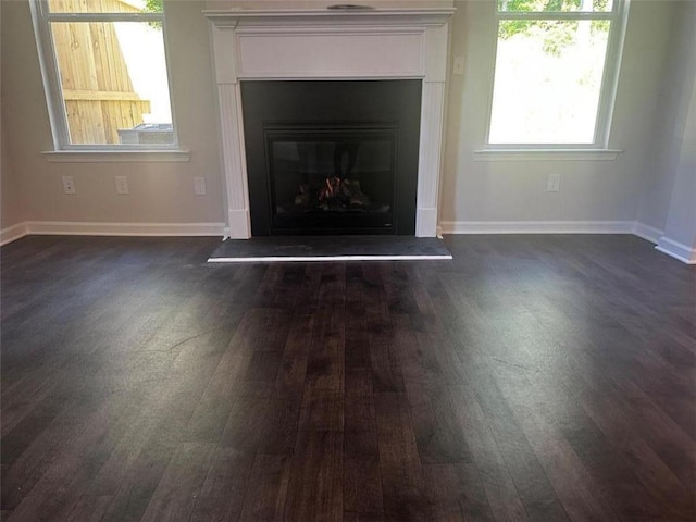 unfurnished living room with dark wood finished floors, a glass covered fireplace, and baseboards