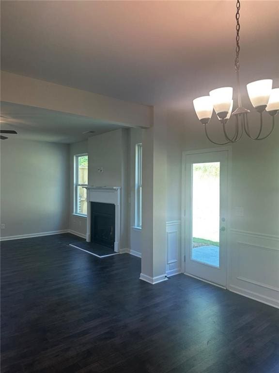 unfurnished living room featuring dark wood finished floors, a chandelier, a fireplace with raised hearth, and baseboards