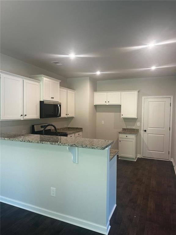 kitchen featuring stainless steel microwave, stone countertops, electric range, a peninsula, and dark wood-type flooring