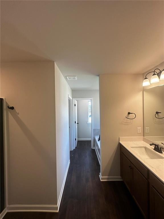 bathroom with wood finished floors, baseboards, vanity, and a tub