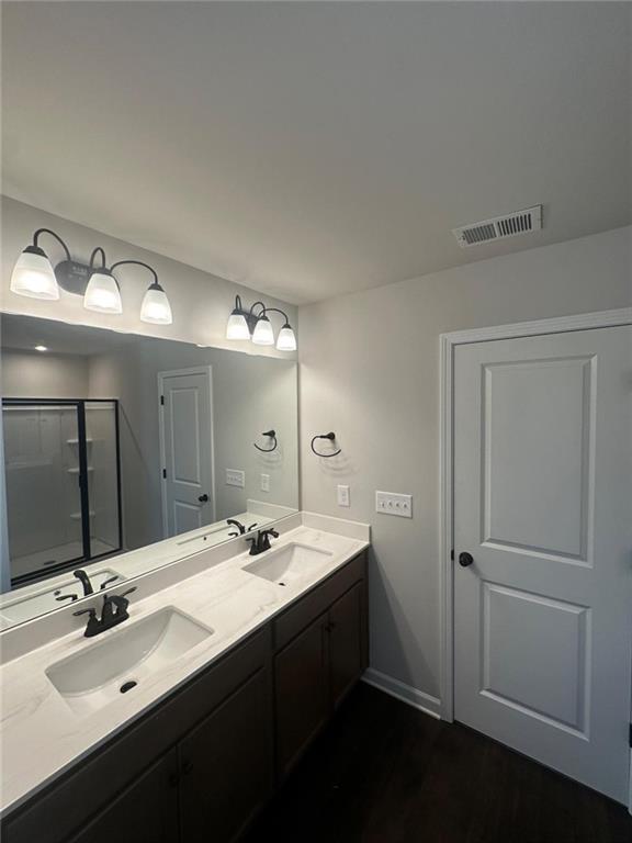 bathroom with double vanity, an enclosed shower, wood finished floors, and baseboards