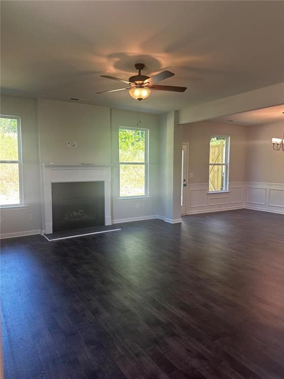 unfurnished living room with a fireplace with raised hearth, healthy amount of natural light, a ceiling fan, a wainscoted wall, and a decorative wall