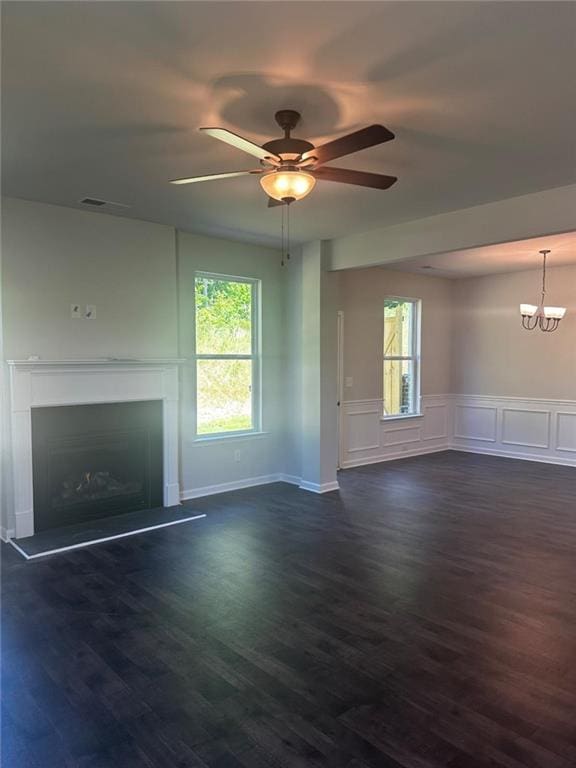 unfurnished living room featuring ceiling fan, a fireplace with raised hearth, plenty of natural light, a chandelier, and wainscoting
