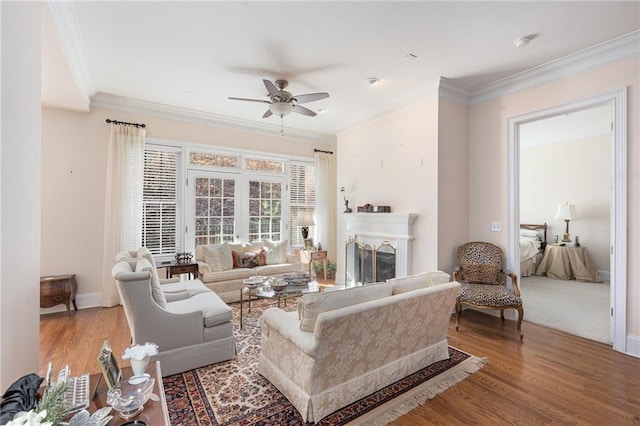 living area with ceiling fan, ornamental molding, wood finished floors, a fireplace, and baseboards