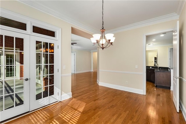 unfurnished dining area with a notable chandelier, crown molding, wood-type flooring, and french doors