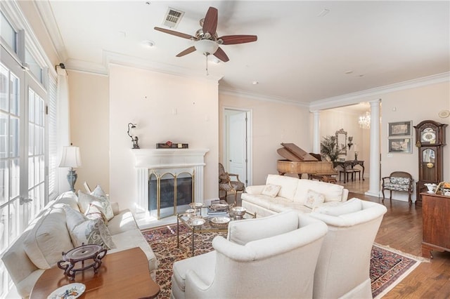 living area with wood finished floors, a ceiling fan, crown molding, ornate columns, and a fireplace
