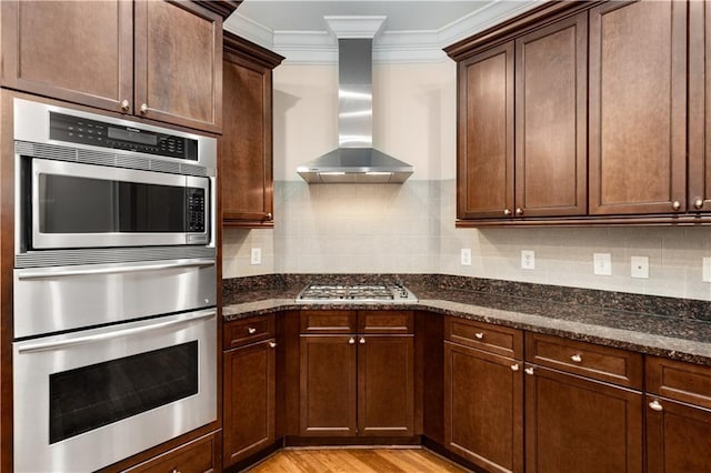 kitchen featuring wall chimney range hood, stainless steel appliances, ornamental molding, decorative backsplash, and dark stone counters