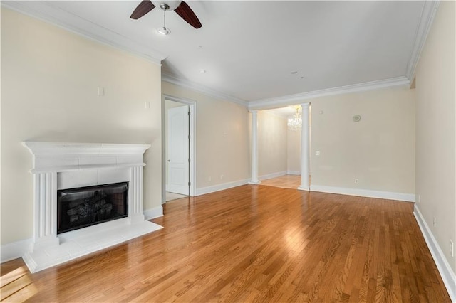 unfurnished living room featuring a ceiling fan, crown molding, light wood-type flooring, a fireplace with raised hearth, and ornate columns