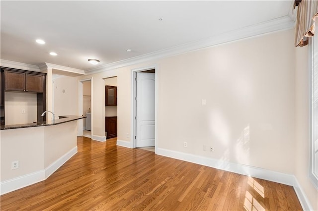 kitchen with hardwood / wood-style floors, washer / dryer, dark stone counters, ornamental molding, and dark brown cabinetry