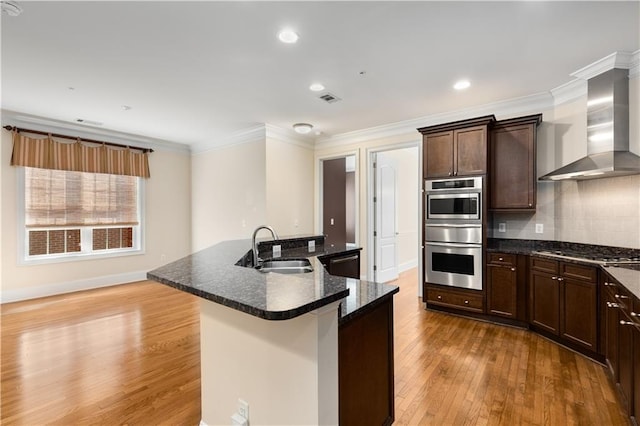 kitchen featuring wall chimney exhaust hood, a sink, stainless steel gas stovetop, light wood finished floors, and black dishwasher