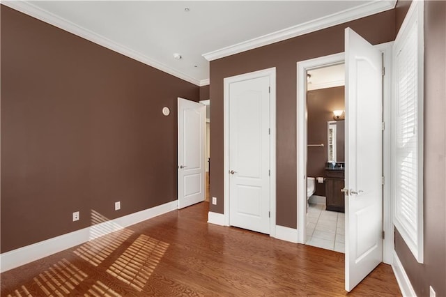 unfurnished bedroom featuring baseboards, ornamental molding, wood finished floors, and connected bathroom