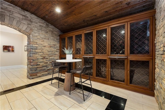 wine area featuring wooden ceiling, vaulted ceiling, tile patterned floors, baseboards, and arched walkways