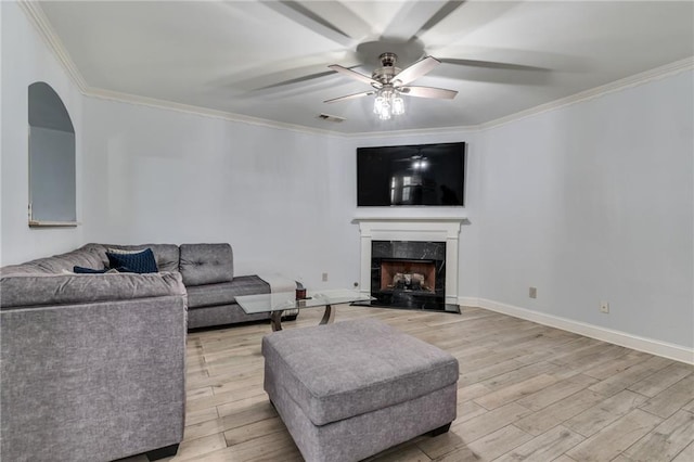 living room with a ceiling fan, a fireplace, light wood-style flooring, visible vents, and ornamental molding