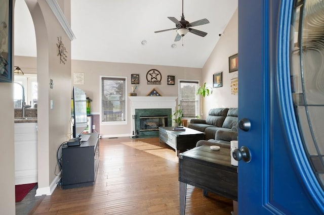 living room with ceiling fan, a high end fireplace, hardwood / wood-style flooring, and high vaulted ceiling