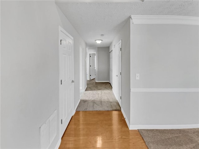 hall with wood-type flooring, a textured ceiling, and ornamental molding