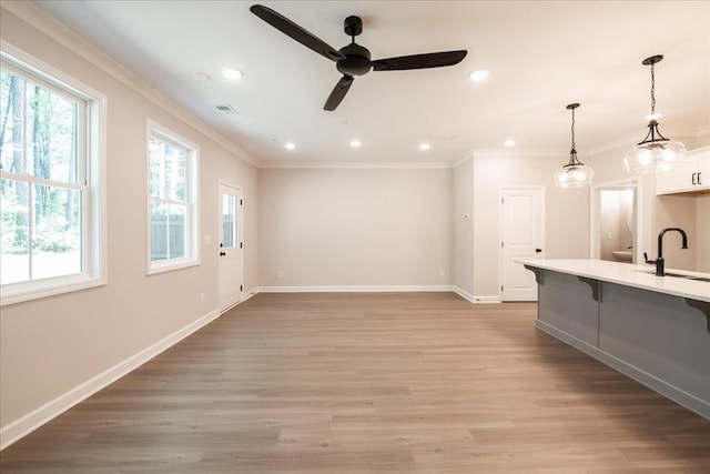 unfurnished living room featuring plenty of natural light, crown molding, a sink, ceiling fan, and baseboards