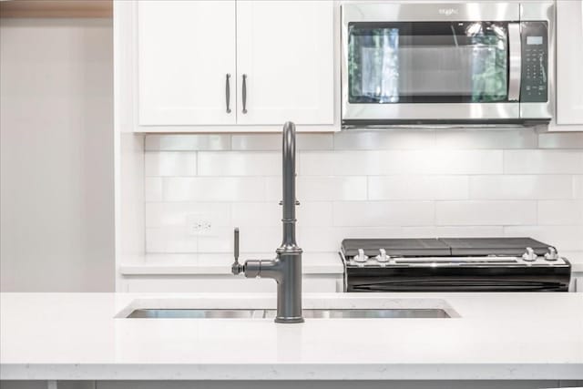 kitchen view of stainless steel microwave, a sink, backsplash, and white cabinetry