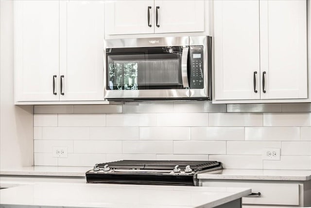 kitchen with stainless steel microwave, backsplash, white cabinets, and light stone counters