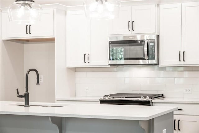 kitchen with stainless steel microwave, a sink, tasteful backsplash, and white cabinets