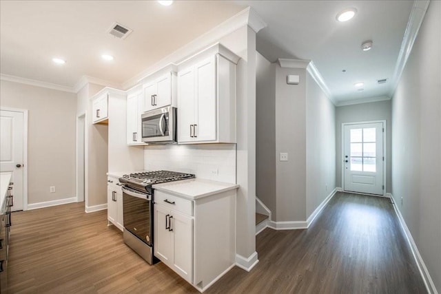 kitchen featuring appliances with stainless steel finishes, ornamental molding, dark wood-style flooring, tasteful backsplash, and white cabinets