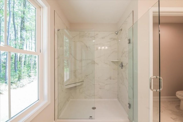 bathroom featuring toilet, a marble finish shower, healthy amount of natural light, and baseboards