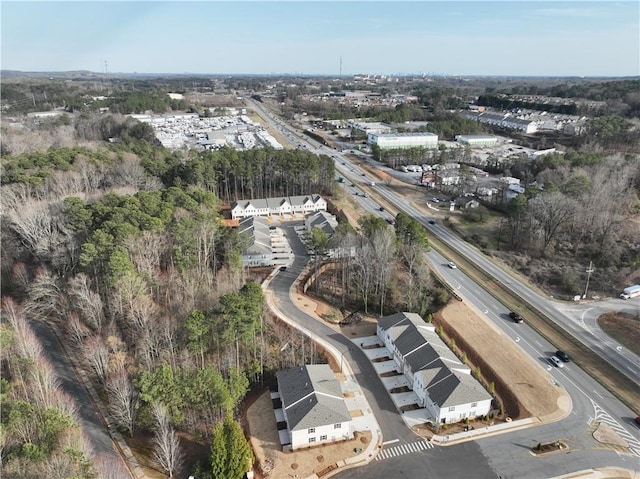 aerial view of property and surrounding area featuring a major roadway and a tree filled landscape