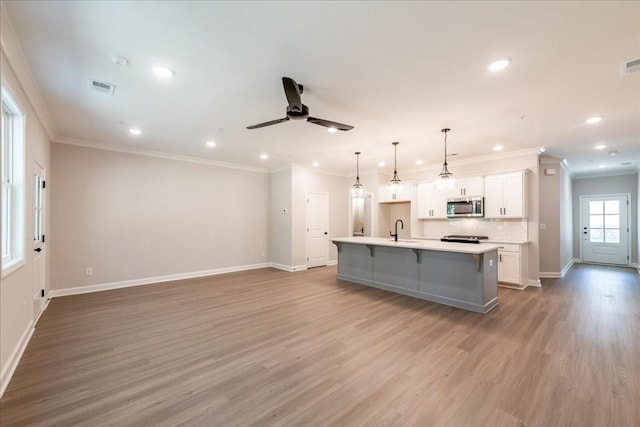 kitchen with stainless steel microwave, a sink, light wood-style flooring, baseboards, and a kitchen island with sink