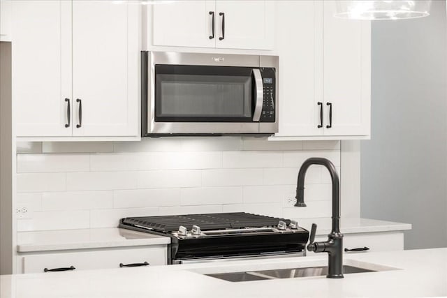 kitchen featuring stainless steel microwave, light countertops, white cabinets, backsplash, and a sink