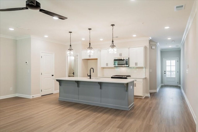 kitchen featuring stainless steel microwave, wood finished floors, white cabinetry, baseboards, and ornamental molding