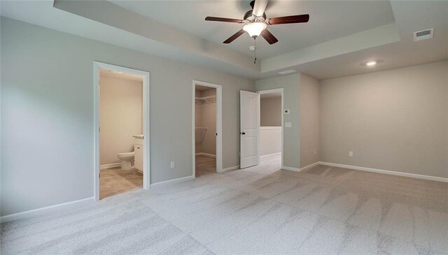 unfurnished bedroom with light carpet, ceiling fan, a spacious closet, connected bathroom, and a closet