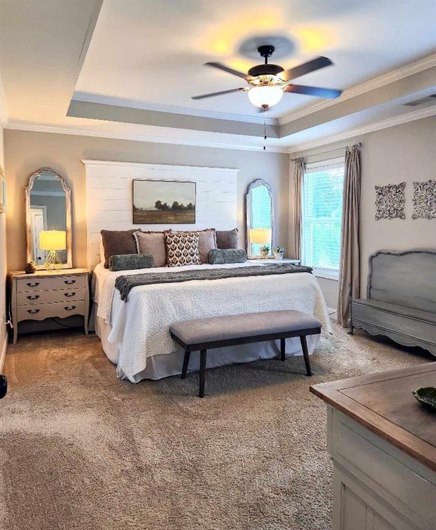 bedroom with a raised ceiling, ceiling fan, carpet flooring, and crown molding