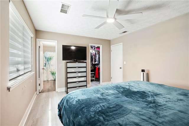 bedroom with ensuite bath, light hardwood / wood-style flooring, ceiling fan, a spacious closet, and a closet