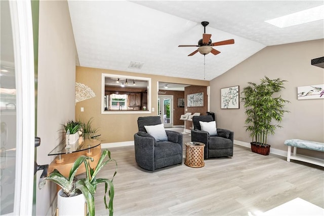 living room with light hardwood / wood-style flooring, ceiling fan, and vaulted ceiling with skylight