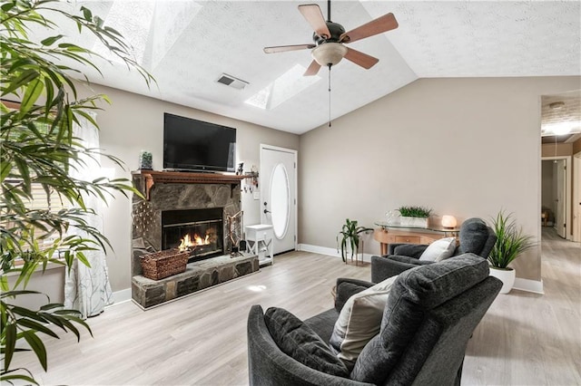 living room with a fireplace, light hardwood / wood-style flooring, ceiling fan, and vaulted ceiling with skylight