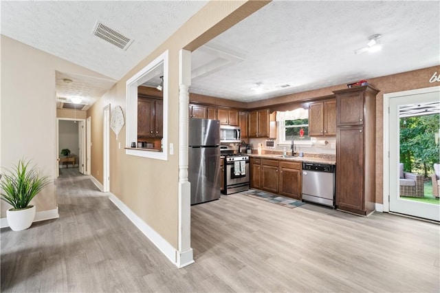 kitchen featuring a textured ceiling, stainless steel appliances, vaulted ceiling, sink, and light hardwood / wood-style flooring