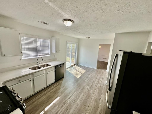 kitchen featuring dishwashing machine, gas stove, freestanding refrigerator, a sink, and light wood-style floors