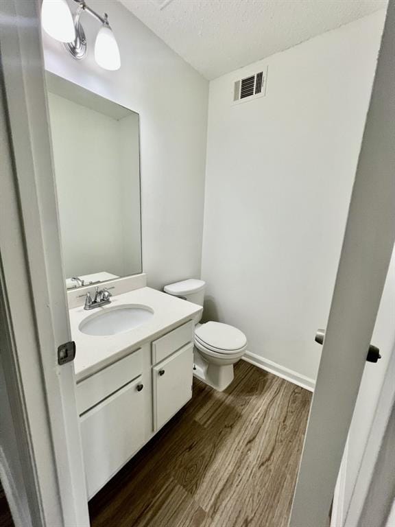 bathroom with visible vents, toilet, vanity, wood finished floors, and a textured ceiling