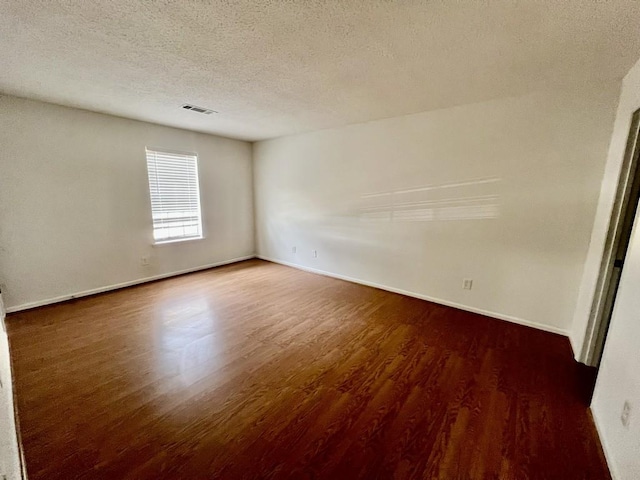 empty room featuring visible vents, baseboards, a textured ceiling, and wood finished floors