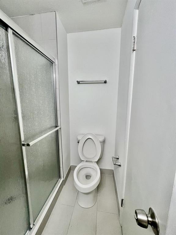 bathroom with tile patterned floors, baseboards, toilet, and a shower stall