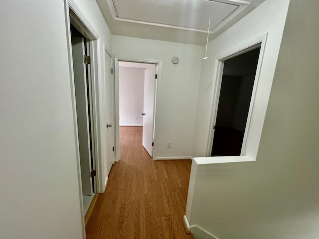 corridor featuring attic access, wood finished floors, and baseboards