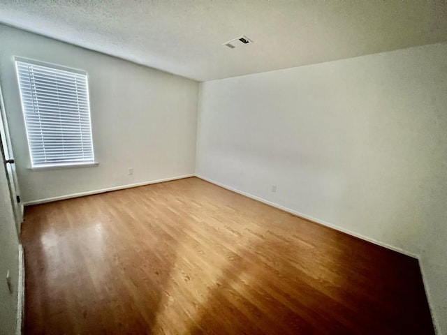 unfurnished room featuring a textured ceiling, wood finished floors, visible vents, and baseboards