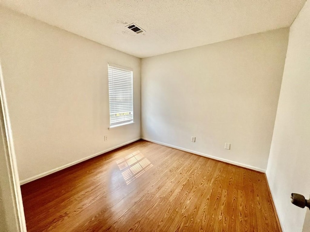 spare room featuring visible vents, a textured ceiling, baseboards, and wood finished floors