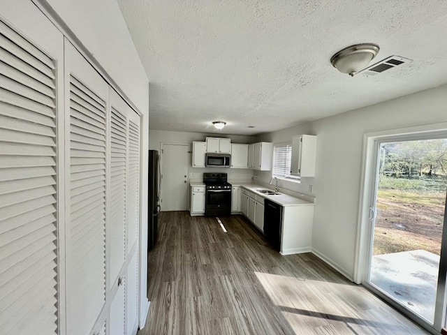 kitchen with visible vents, dark wood finished floors, light countertops, white cabinets, and black appliances