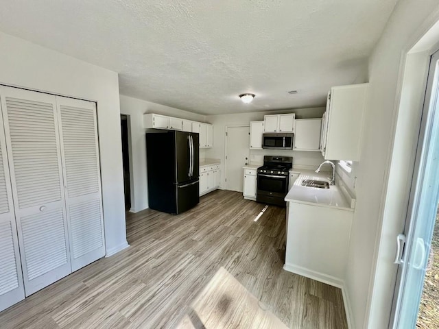 kitchen with light wood-style flooring, a sink, white cabinetry, stainless steel appliances, and light countertops