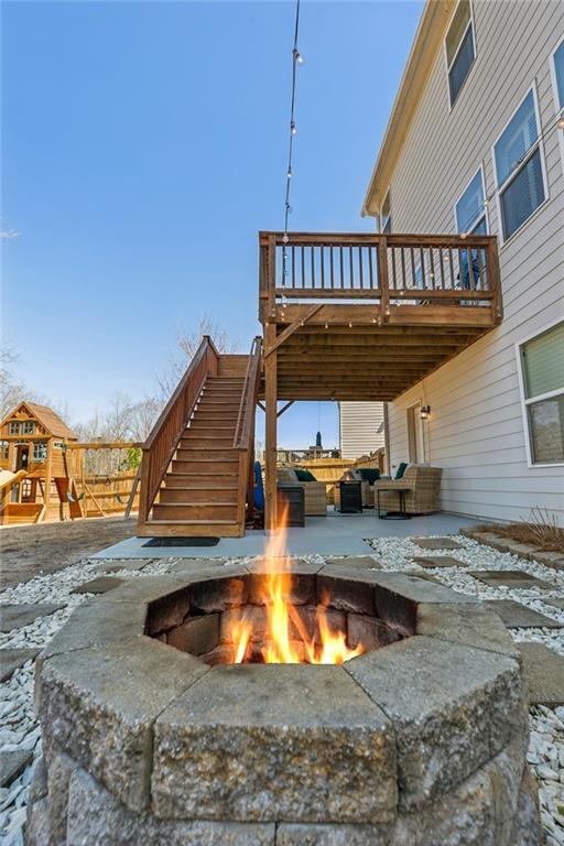 view of patio with a wooden deck, stairway, a playground, and an outdoor fire pit