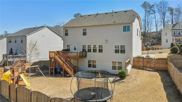 back of property with a wooden deck, a trampoline, a fenced backyard, and a playground